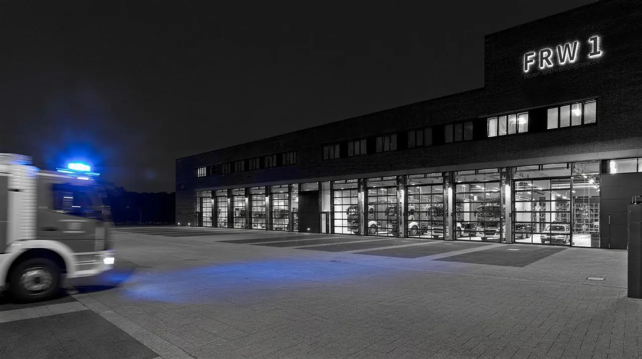 Feuer- und Rettungswache 1 Hannover bei Nacht in Schwarz-Weiß – vollverglaste Sektionaltore von Hild-Moser, links ein ausrückendes Einsatzfahrzeug mit blauem Signallicht